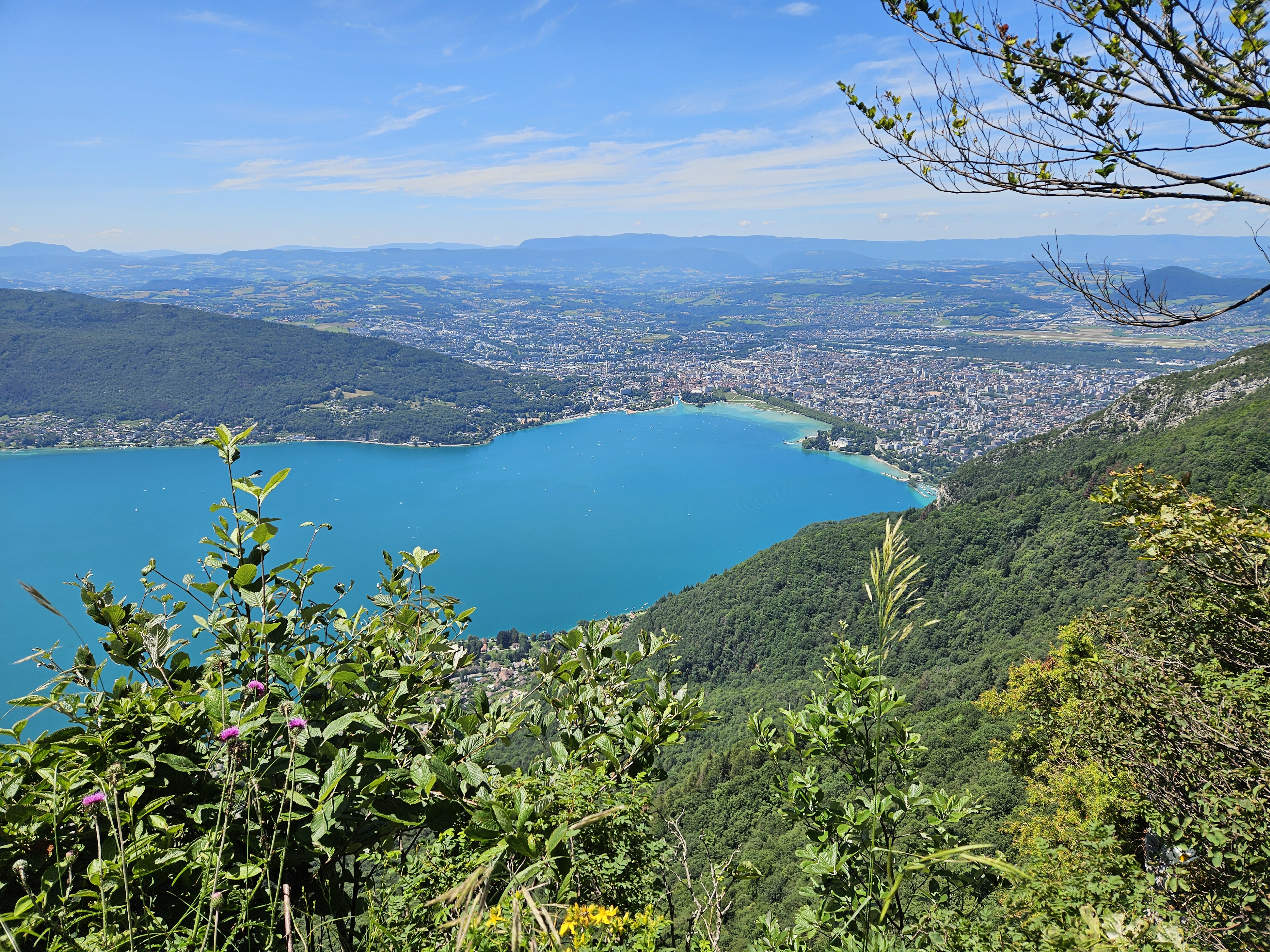 An overhead view, looking down from a greenery-covered mountainside, of a sprawling town along the shores of an almost painfully blue lake.