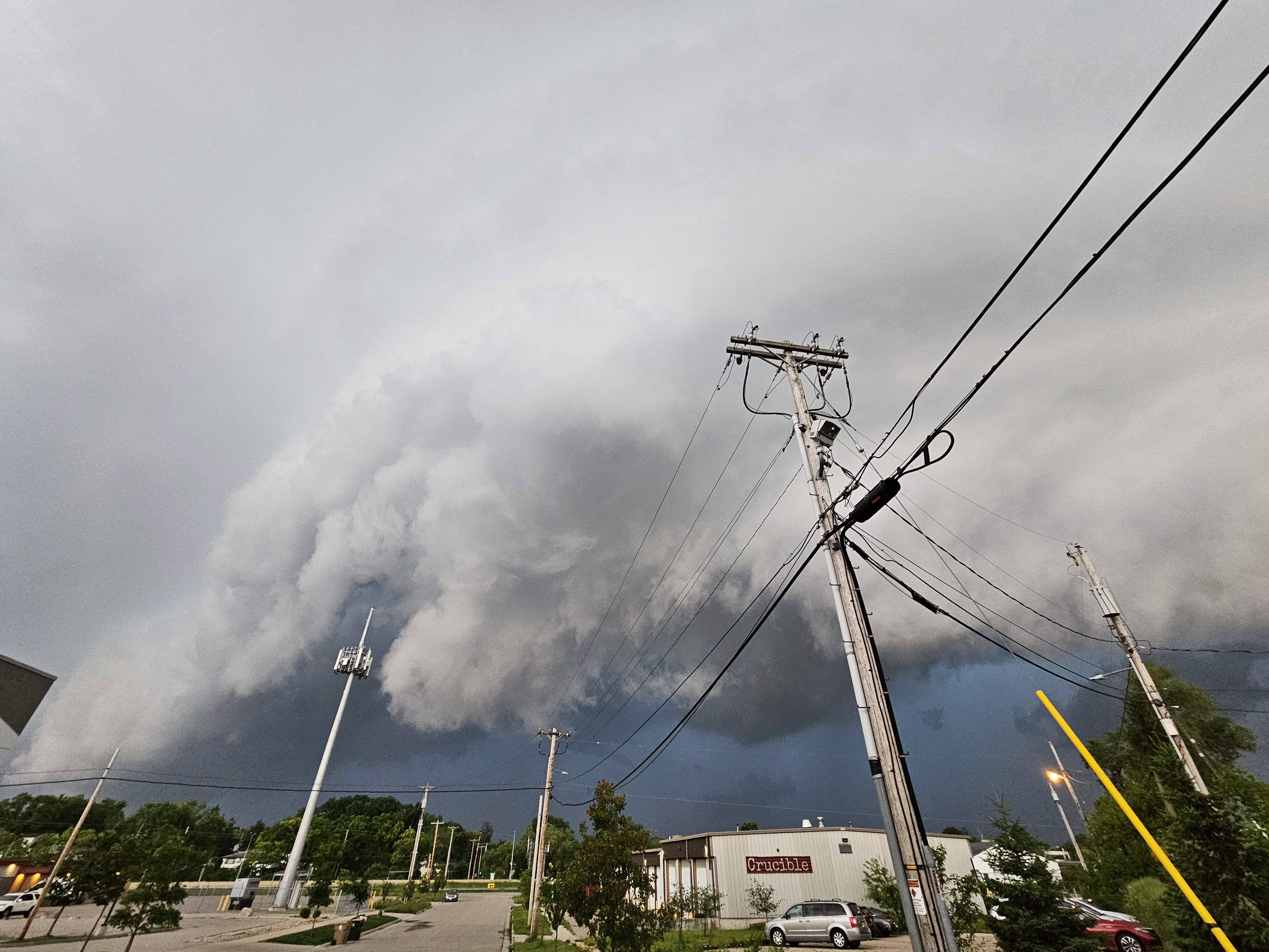 A large wall cloud looms over darker skies. Underneath, a city street and utility poles line the warehouse where the nightclub Crucible is housed.