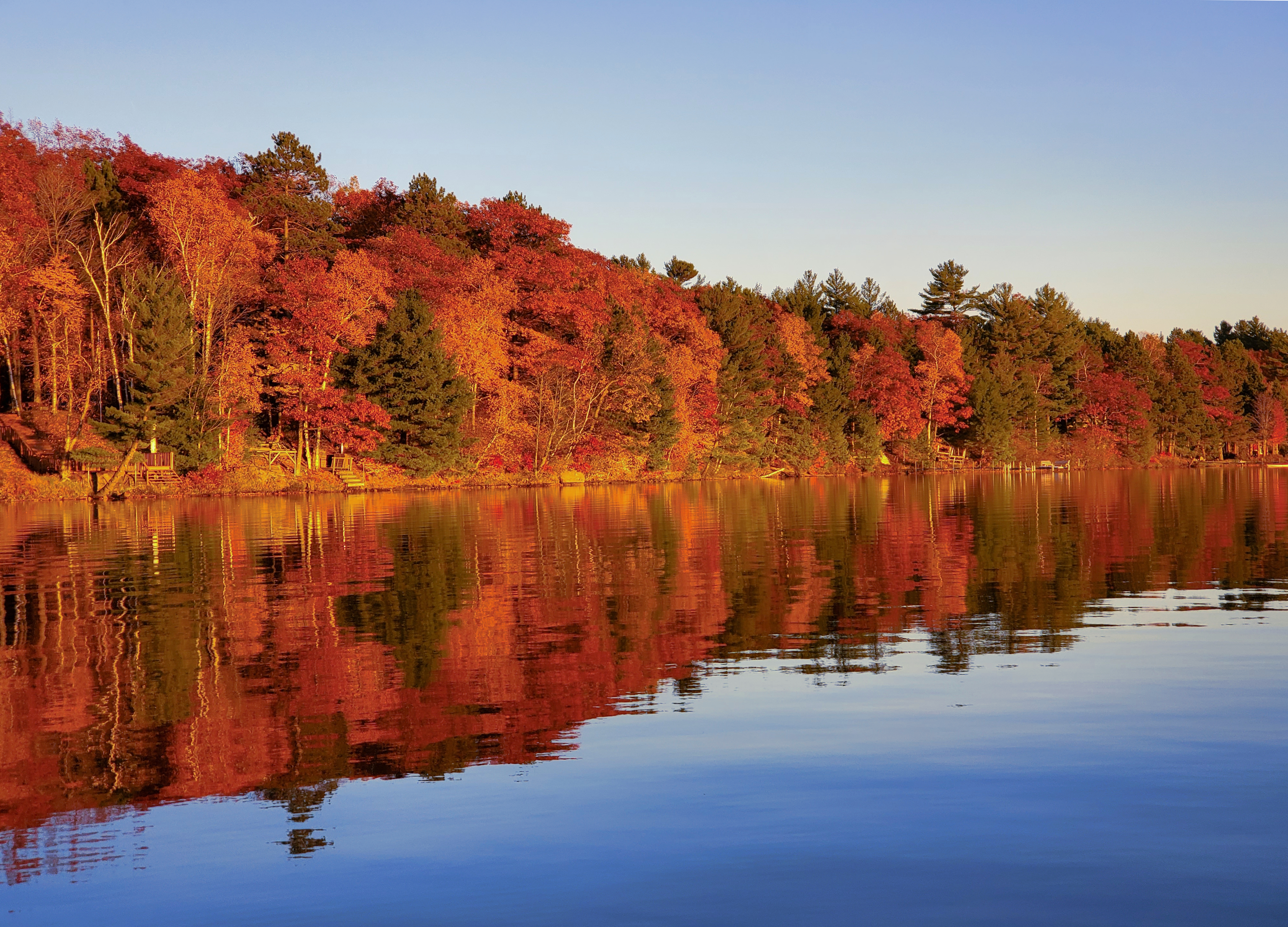 Brightly colored autumn leaves on trees line a placid lake, where the reflected reds, yellows, and greens can be seen clearly in the water, too.