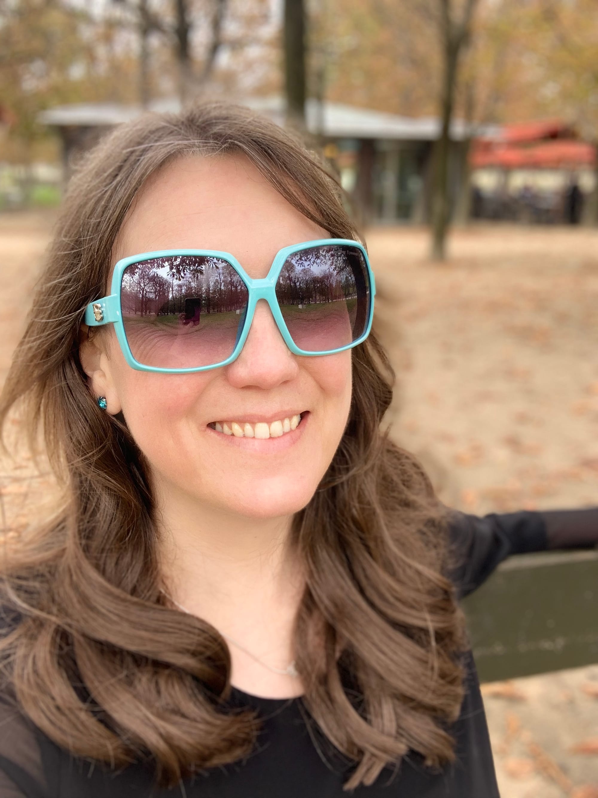 A white woman with long, light brown hair and wearing large sunglasses smiles into the camera.