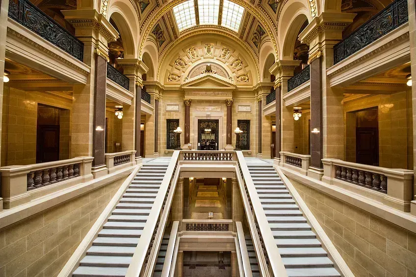 Two, side-by-side staircases leaded up to an ornate doorway, flanked on either side by hallways lined with tall columns.