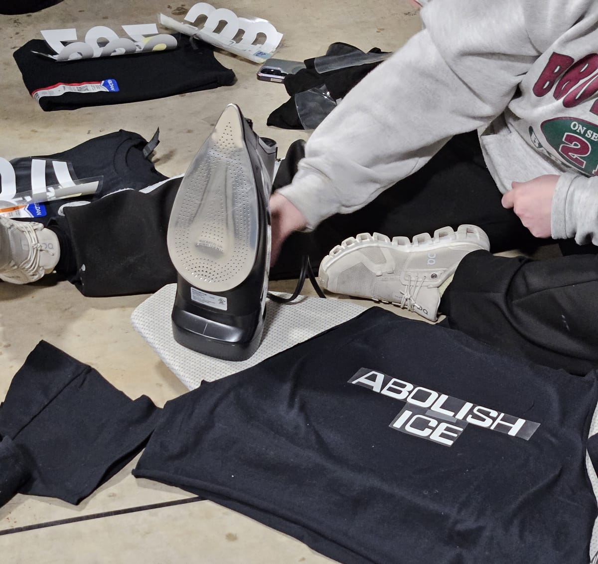 Close-up shot of a person using a hot iron to put text on a black t-shirt. The text reads, "Abolish ICE."