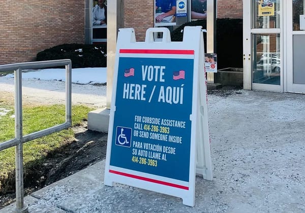 A sandwich board sign reads “Vote Here/Aqui”