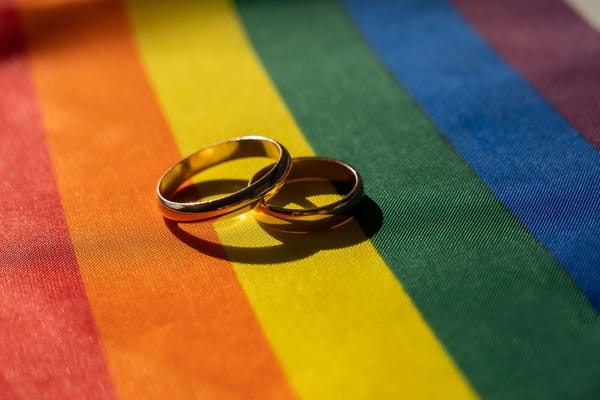 Two simple gold wedding bands on top of a rainbow Pride-colored fabric.
