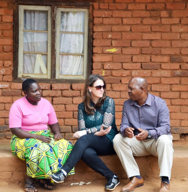 Three people sit along a curb, talking with one another. 