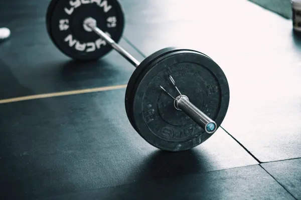 A bar with large round weights mounted on either end, set on top of black gym mats.